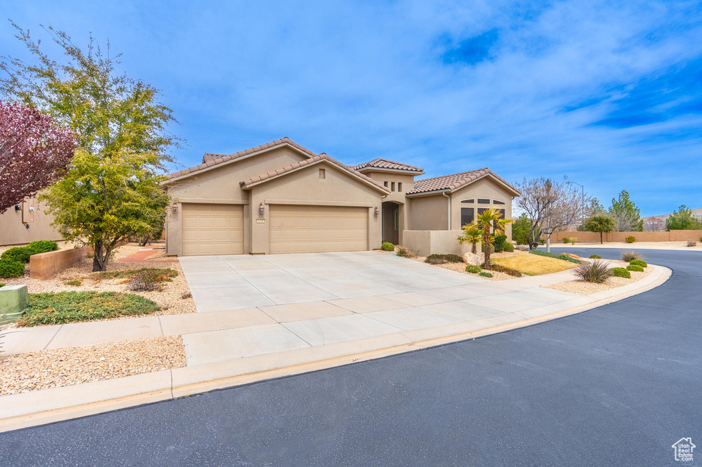 Mediterranean / spanish home featuring stucco siding, a tile roof, a garage, and driveway