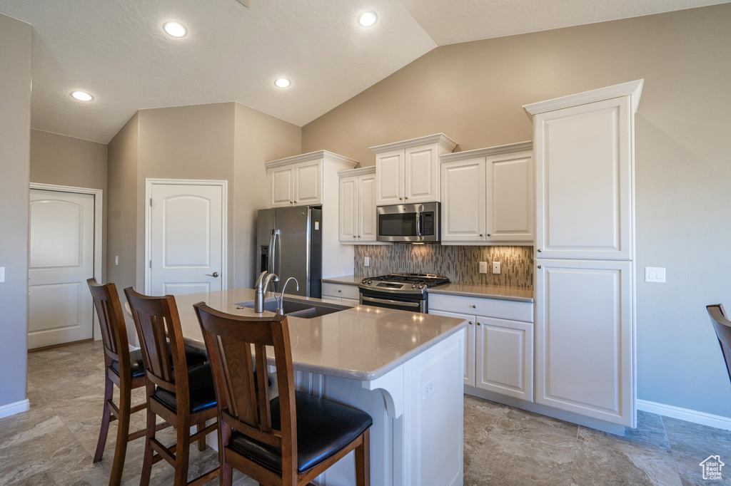 Kitchen with a kitchen breakfast bar, appliances with stainless steel finishes, an island with sink, a sink, and backsplash
