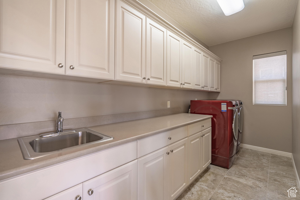 Laundry room with washing machine and clothes dryer, cabinet space, a sink, and baseboards