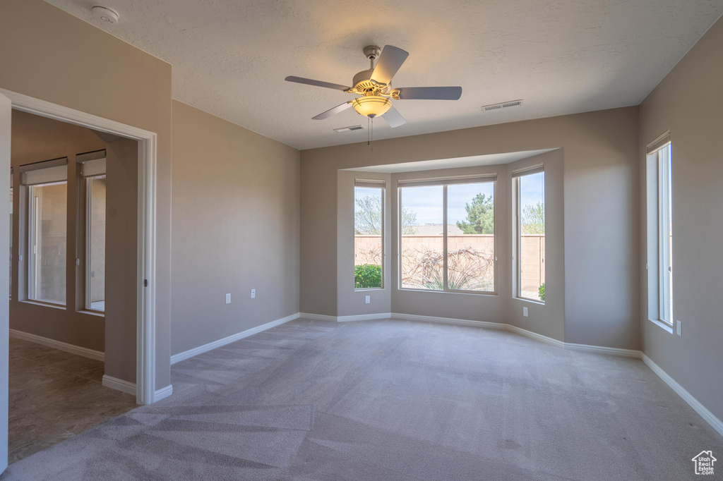 Carpeted empty room with a textured ceiling, baseboards, ceiling fan, and visible vents