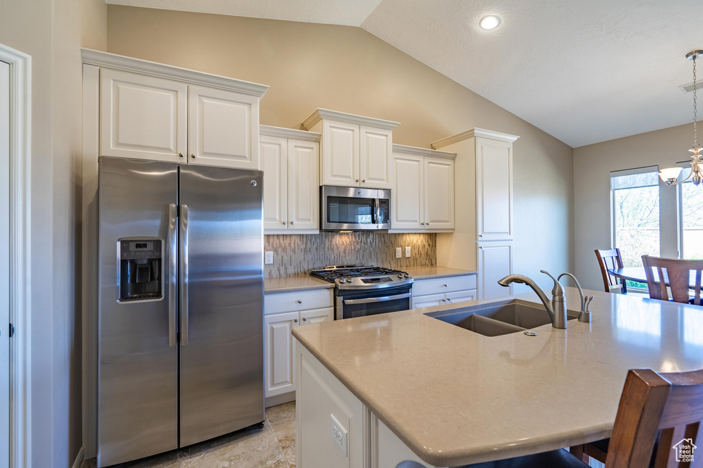 Kitchen with lofted ceiling, an inviting chandelier, decorative backsplash, a sink, and appliances with stainless steel finishes
