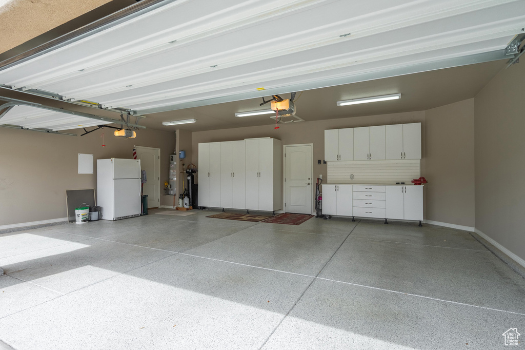 Garage featuring freestanding refrigerator, strapped water heater, baseboards, and a garage door opener