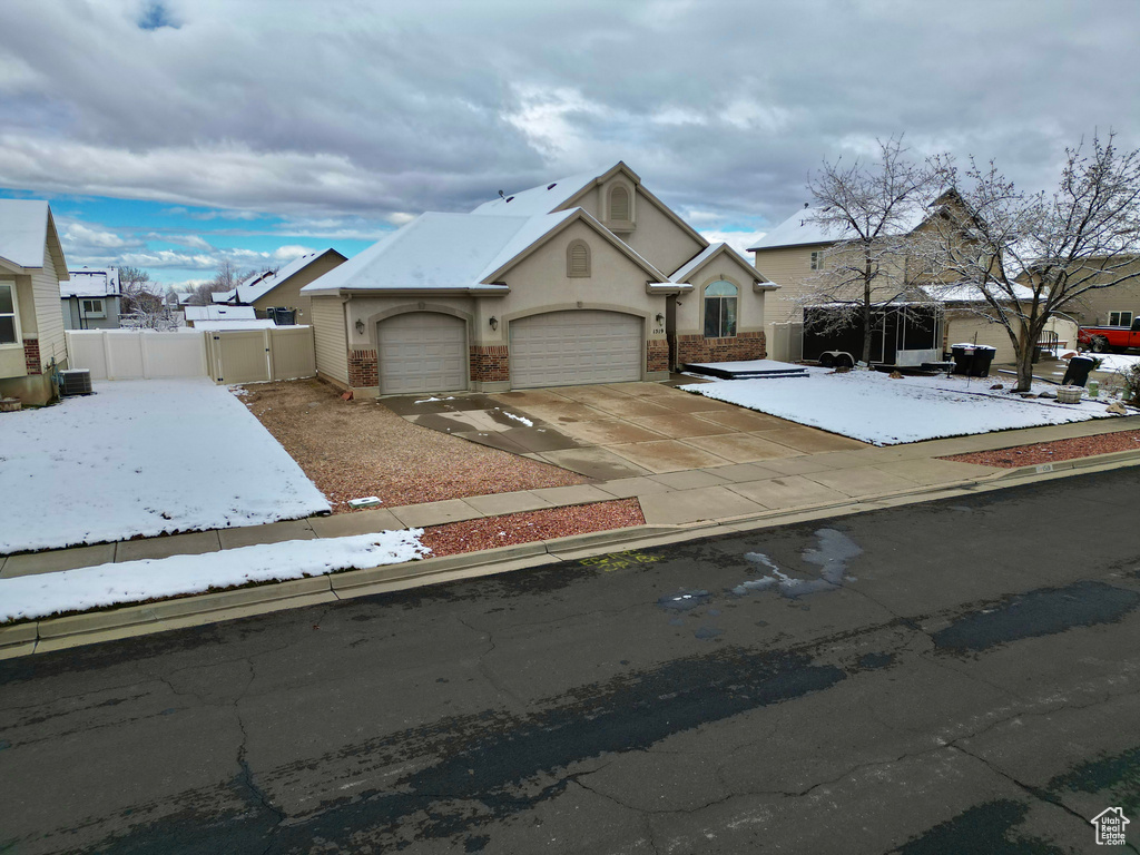 View of front of home with a gate, fence, driveway, central AC, and a garage