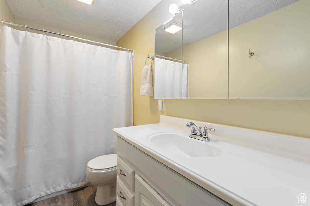 Full bath with toilet, a shower with shower curtain, vanity, wood finished floors, and a textured ceiling