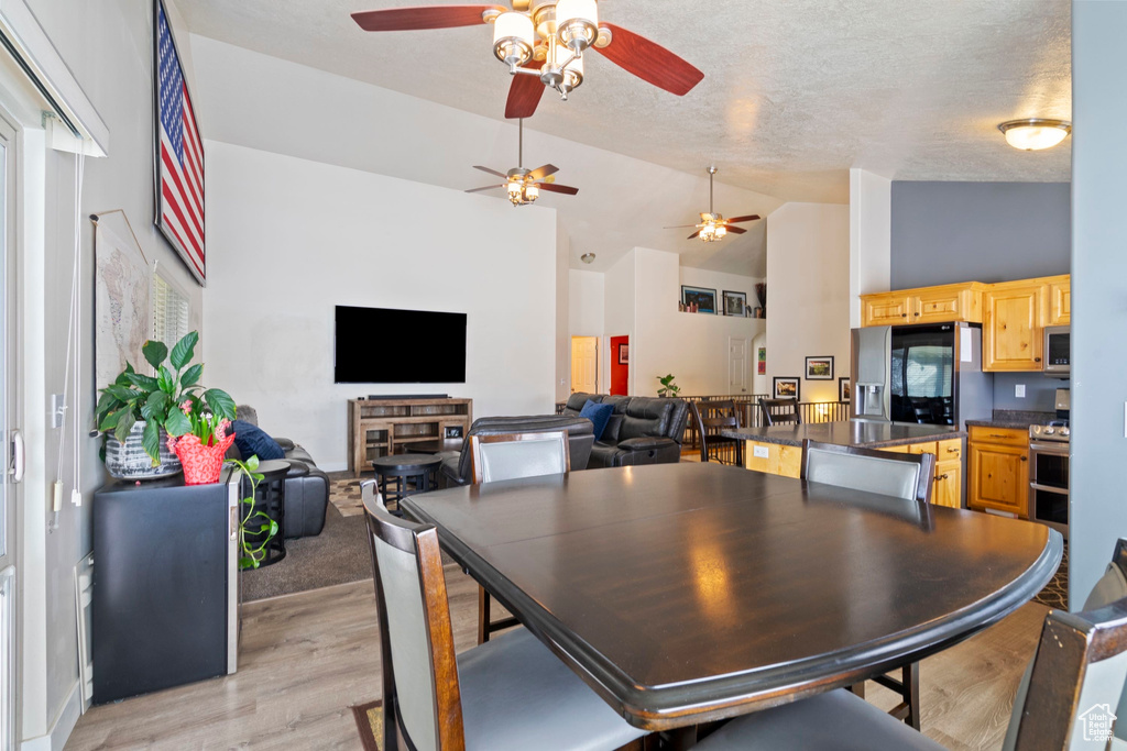 Dining area with high vaulted ceiling, a ceiling fan, light wood finished floors, and a textured ceiling