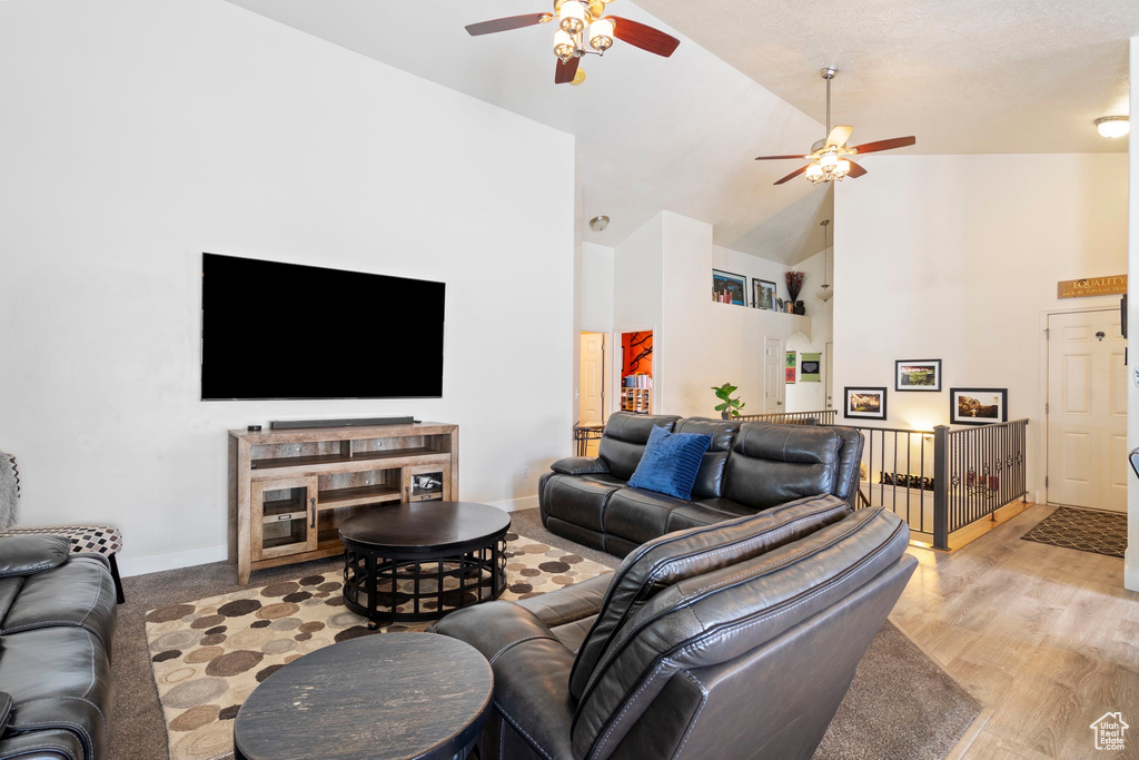 Living room with light wood-style flooring, a ceiling fan, baseboards, and high vaulted ceiling