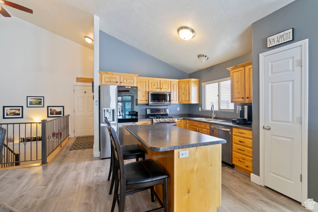 Kitchen featuring dark countertops, a breakfast bar area, stainless steel appliances, a ceiling fan, and a sink