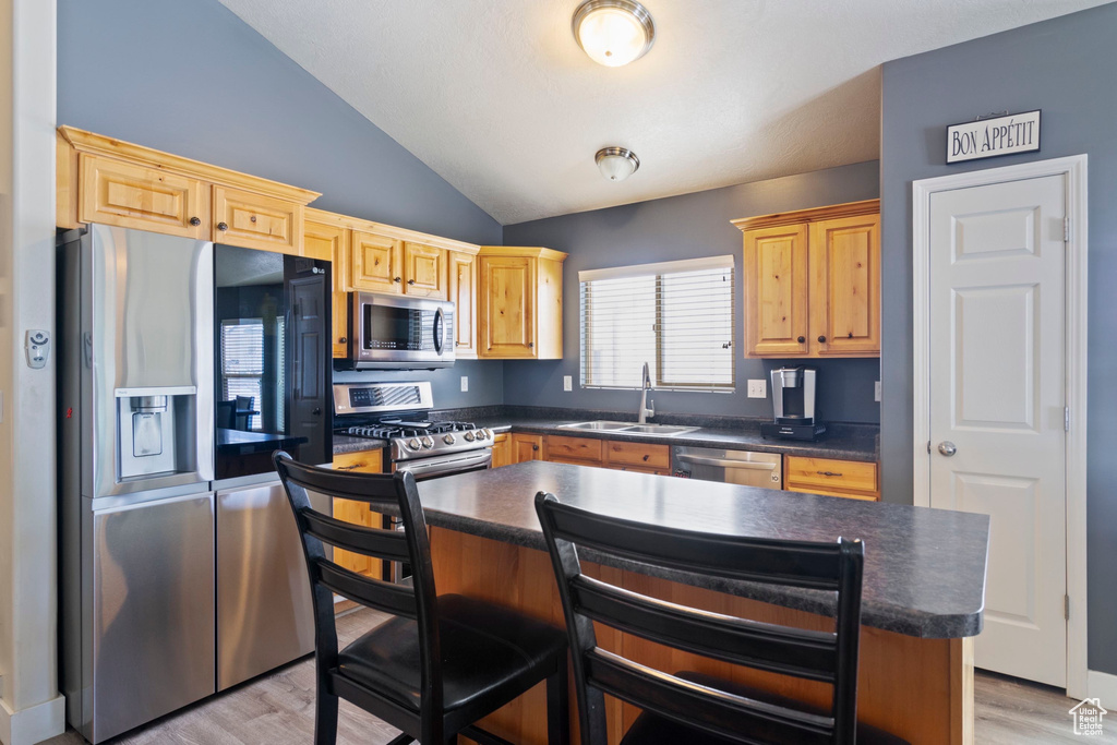 Kitchen featuring dark countertops, vaulted ceiling, appliances with stainless steel finishes, light wood-style floors, and a sink