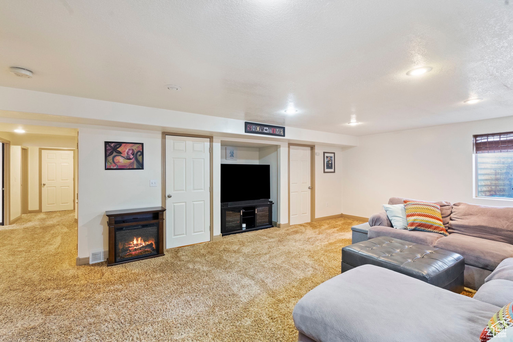 Carpeted living room featuring baseboards, visible vents, recessed lighting, a textured ceiling, and a glass covered fireplace