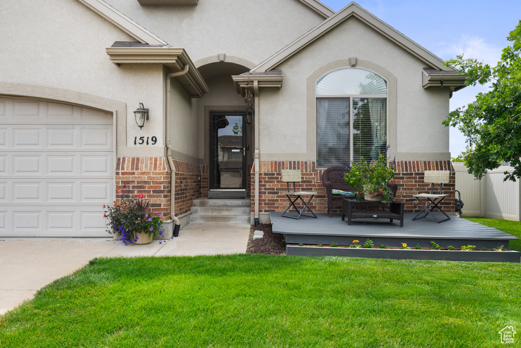View of exterior entry featuring brick siding, a lawn, stucco siding, and a wooden deck