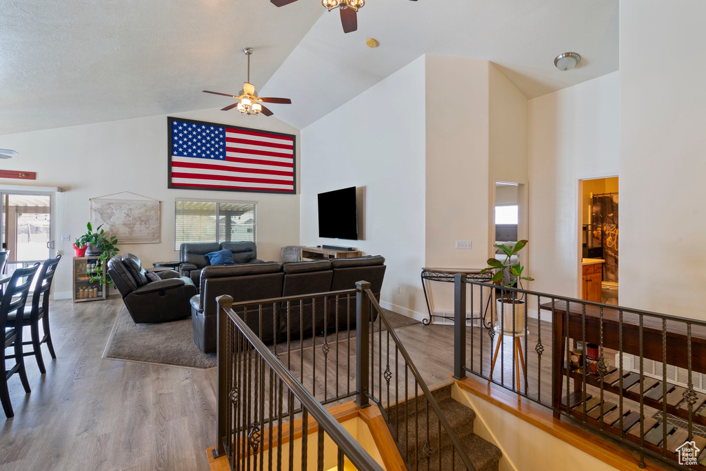 Living room with baseboards, high vaulted ceiling, wood finished floors, and a ceiling fan