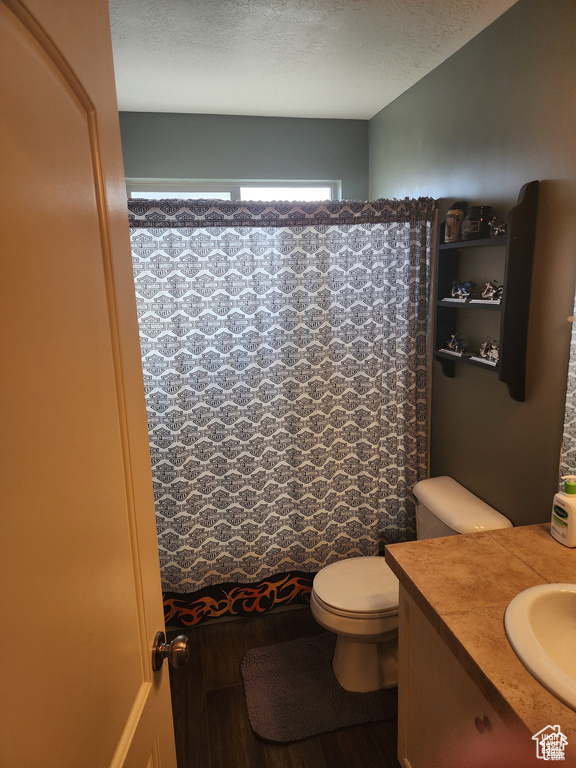 Full bathroom with toilet, curtained shower, a textured ceiling, wood finished floors, and vanity