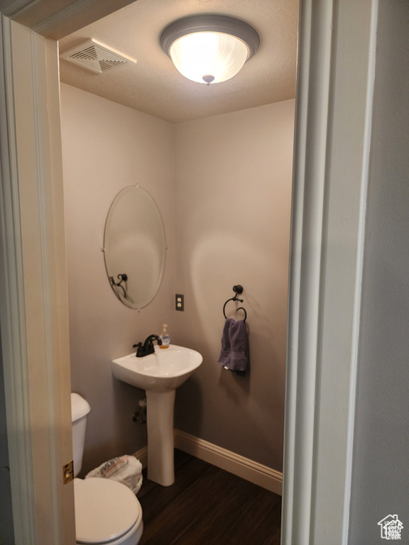 Half bathroom featuring wood finished floors, visible vents, baseboards, a sink, and toilet