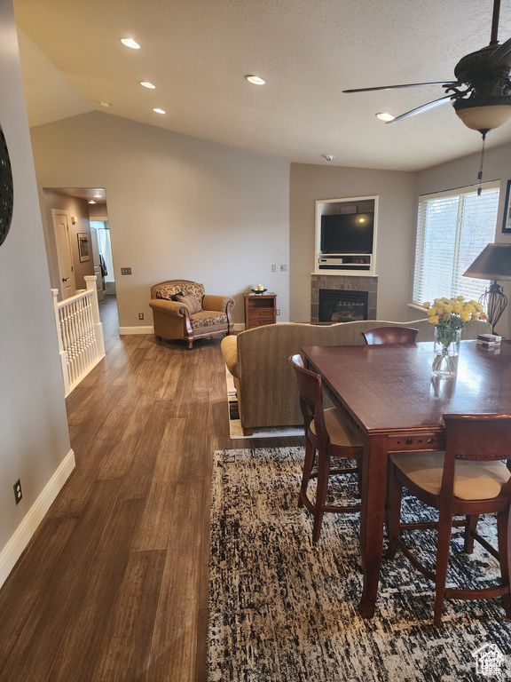 Dining room featuring wood finished floors, baseboards, lofted ceiling, a fireplace, and ceiling fan