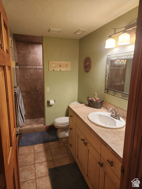 Bathroom with toilet, visible vents, a tile shower, and a textured ceiling