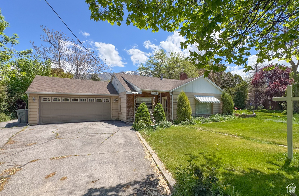 View of front facade featuring a front yard, an attached garage, driveway, a chimney, and stone siding