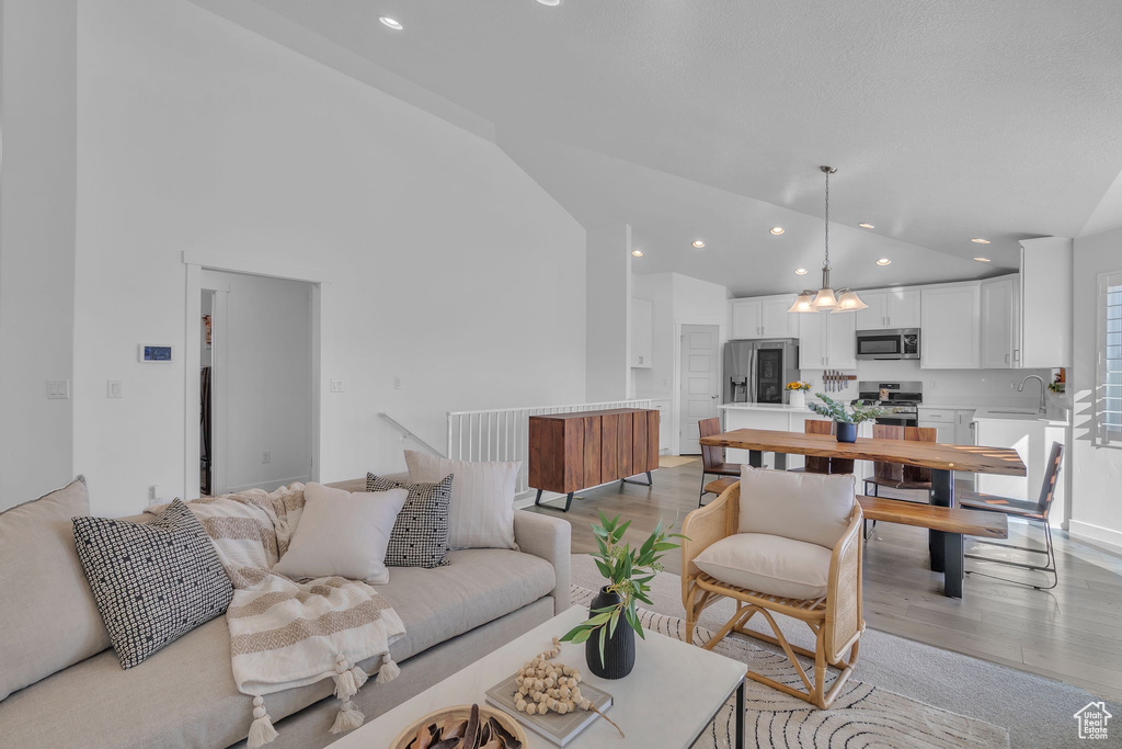 Living room with high vaulted ceiling, an inviting chandelier, recessed lighting, and light wood-type flooring