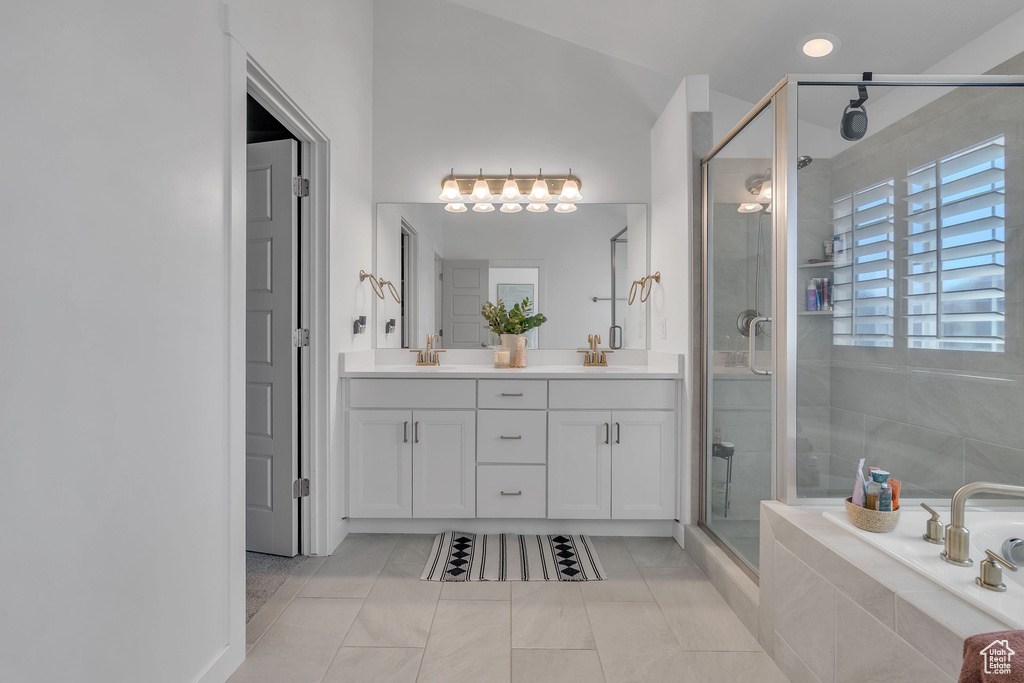 Bathroom featuring a relaxing tiled tub, double vanity, a sink, and a stall shower