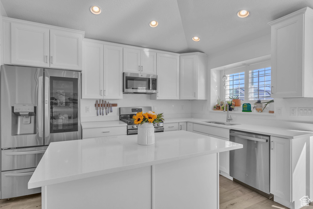 Kitchen with a sink, white cabinetry, appliances with stainless steel finishes, and vaulted ceiling