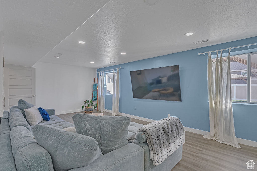 Living area with baseboards, a textured ceiling, visible vents, and wood finished floors
