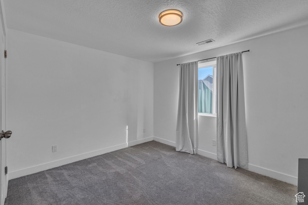 Carpeted empty room with baseboards, a textured ceiling, and visible vents