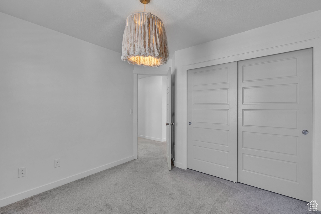 Unfurnished bedroom with an inviting chandelier, a closet, carpet, and baseboards