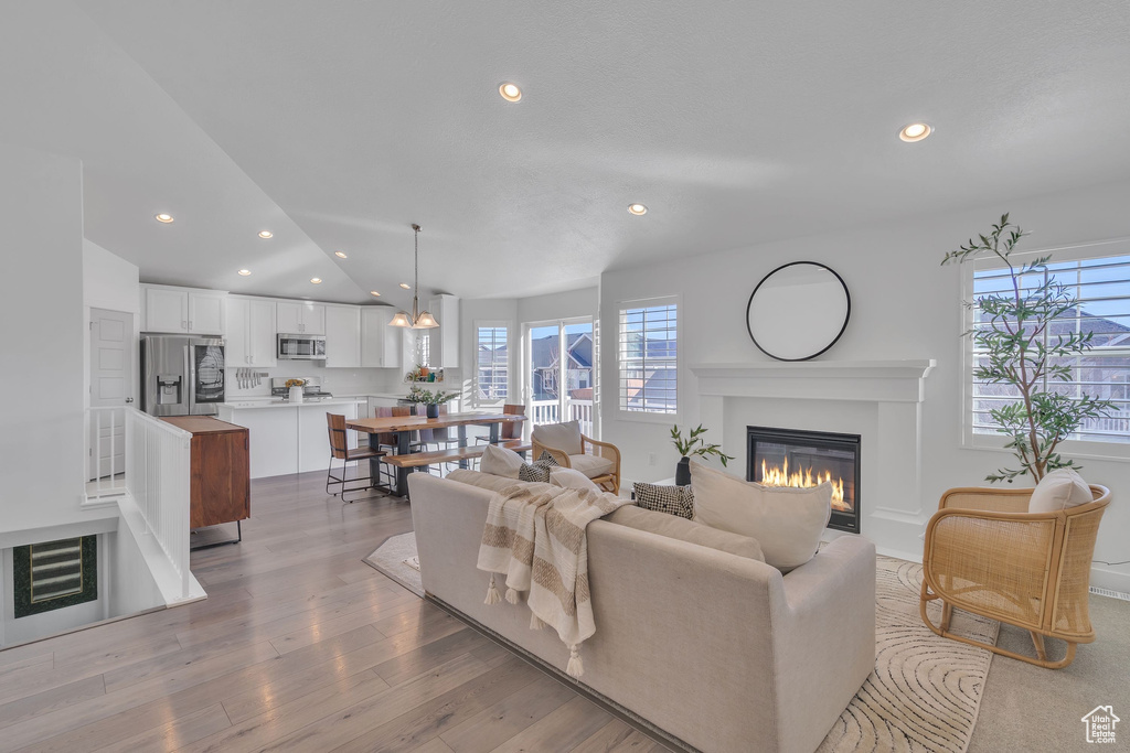Living area with lofted ceiling, a glass covered fireplace, recessed lighting, and light wood finished floors