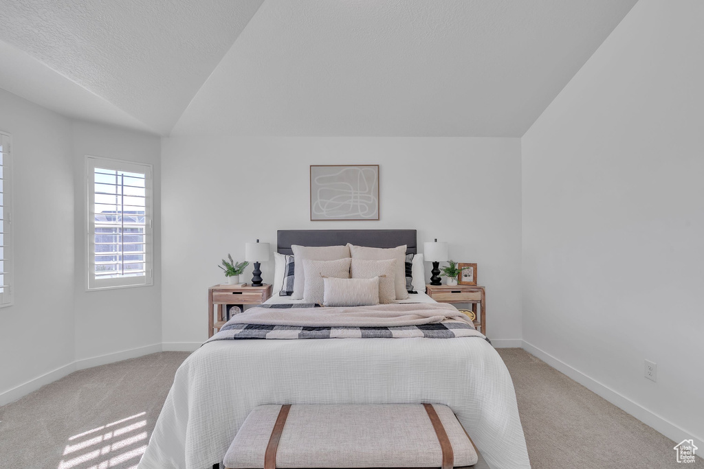 Bedroom with baseboards, vaulted ceiling, and light carpet