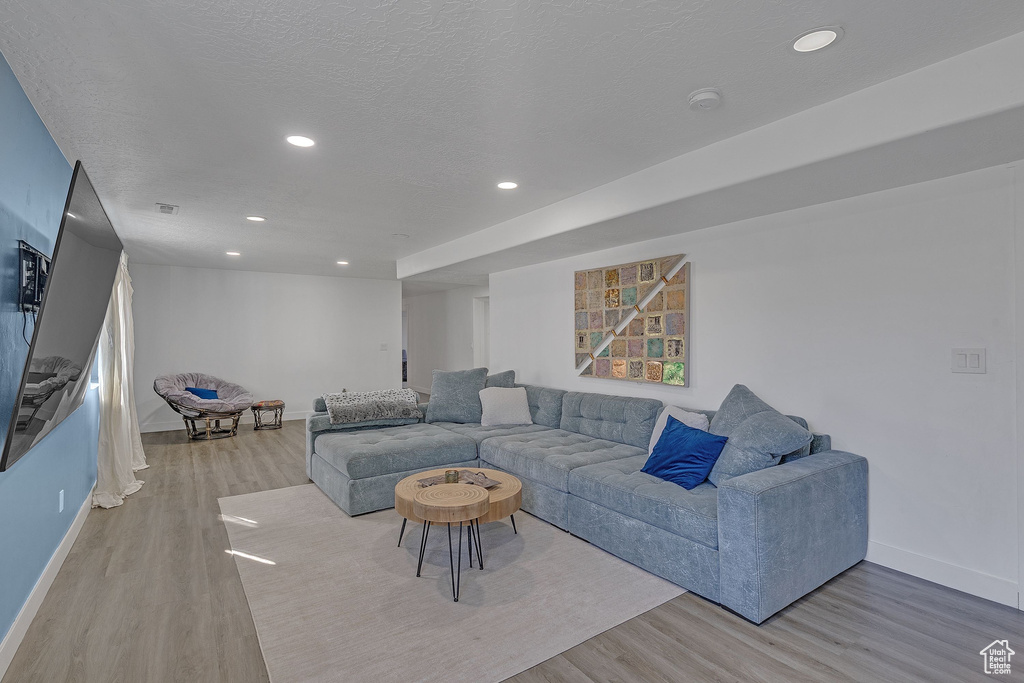Living room featuring a textured ceiling, light wood-type flooring, baseboards, visible vents, and recessed lighting