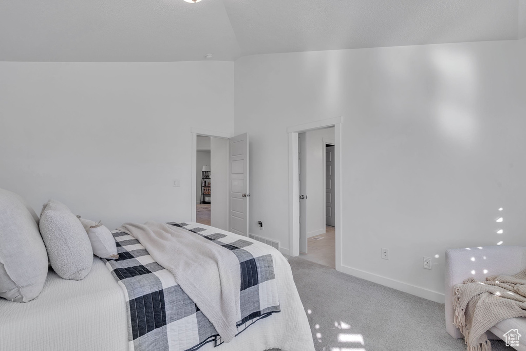 Bedroom featuring baseboards, a high ceiling, visible vents, and light carpet