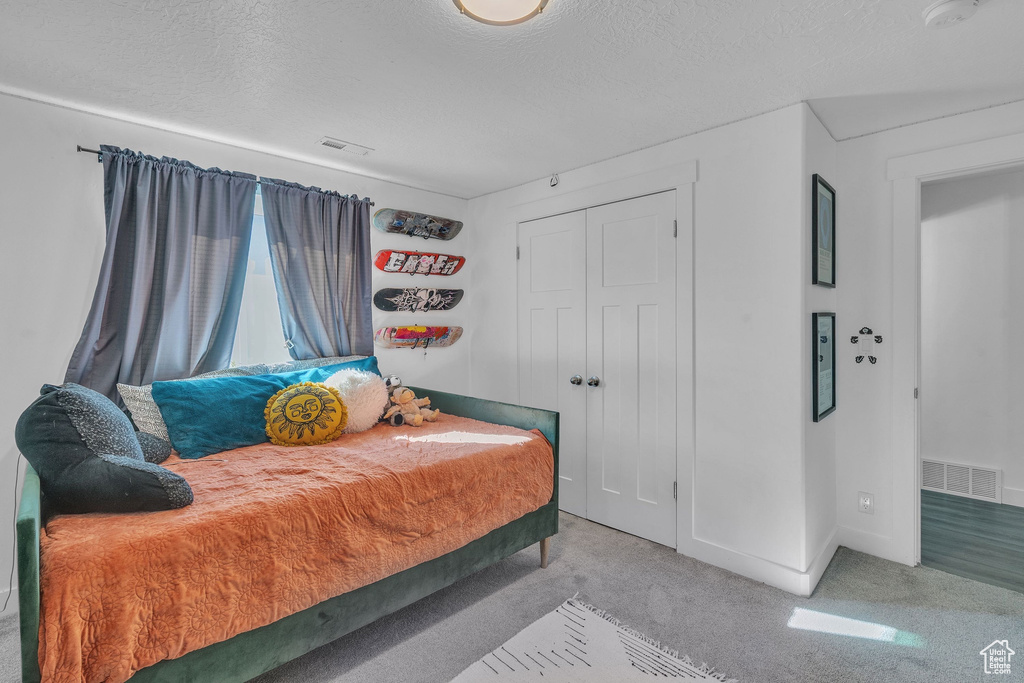 Carpeted bedroom featuring a textured ceiling, a closet, and visible vents