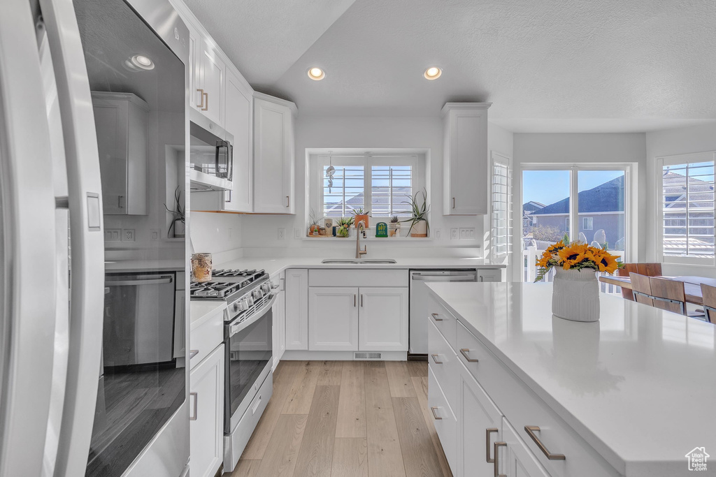 Kitchen with light wood-style flooring, stainless steel appliances, recessed lighting, white cabinetry, and a sink