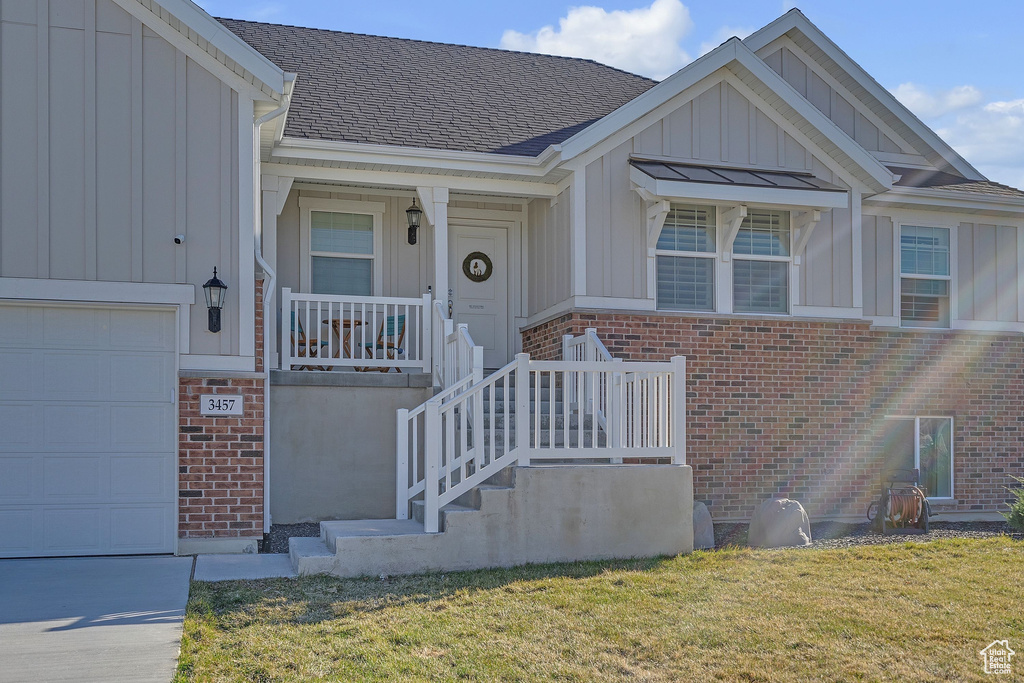 View of front facade featuring a garage, brick siding, board and batten siding, covered porch, and a shingled roof