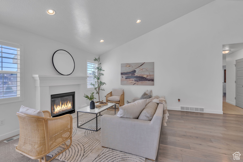 Living area featuring visible vents, vaulted ceiling, a glass covered fireplace, and wood finished floors