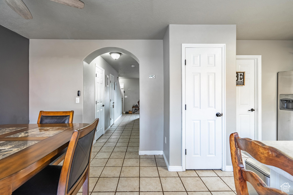 Dining space with light tile patterned floors, arched walkways, baseboards, and ceiling fan
