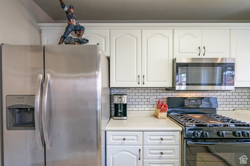 Kitchen featuring light countertops, white cabinets, appliances with stainless steel finishes, and decorative backsplash