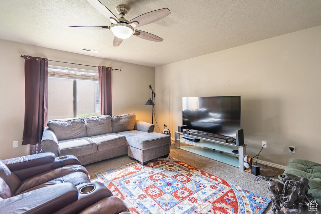 Living room featuring carpet floors, a textured ceiling, baseboards, visible vents, and ceiling fan