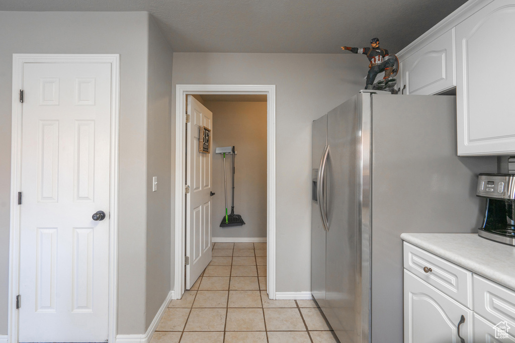 Kitchen with light countertops, stainless steel refrigerator with ice dispenser, light tile patterned floors, baseboards, and white cabinets