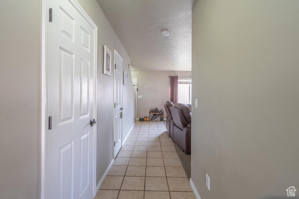 Hall featuring light tile patterned flooring, a textured ceiling, and baseboards