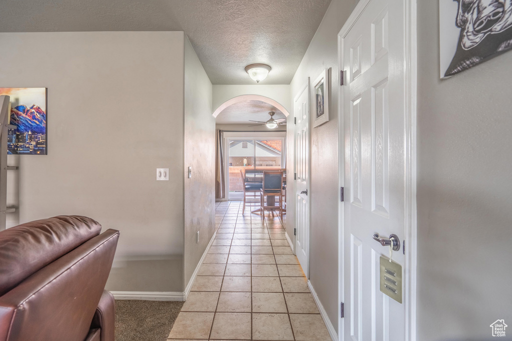 Corridor with light tile patterned flooring, baseboards, arched walkways, and a textured ceiling