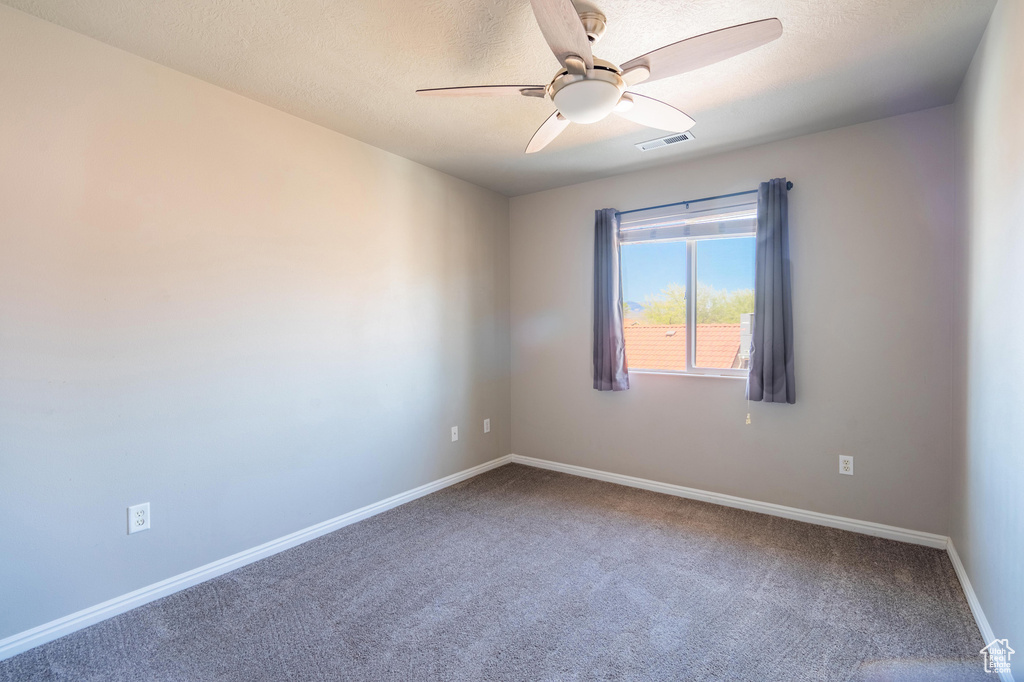 Empty room with a textured ceiling, visible vents, carpet, baseboards, and ceiling fan