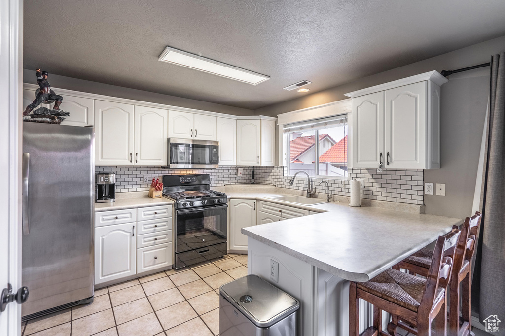 Kitchen featuring a sink, a breakfast bar area, a peninsula, stainless steel appliances, and visible vents