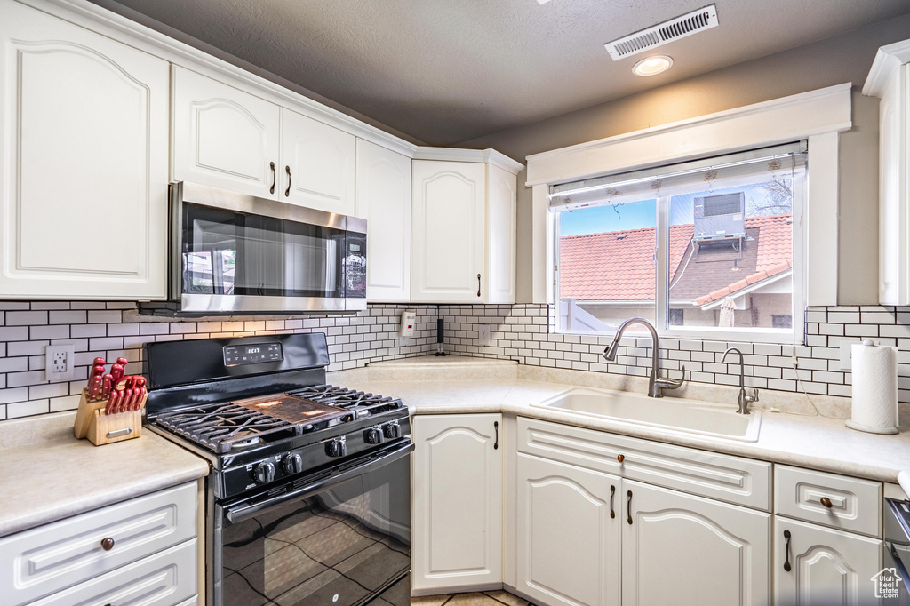 Kitchen featuring white cabinetry, stainless steel microwave, gas stove, a sink, and visible vents