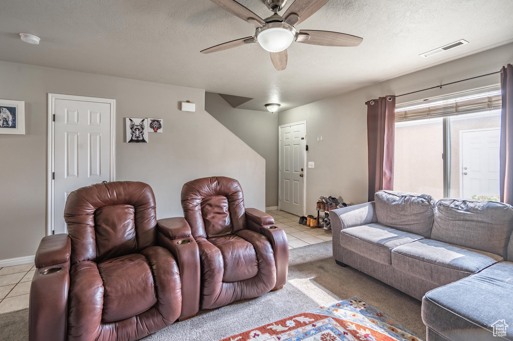 Living room with a textured ceiling, visible vents, light tile patterned floors, and a ceiling fan