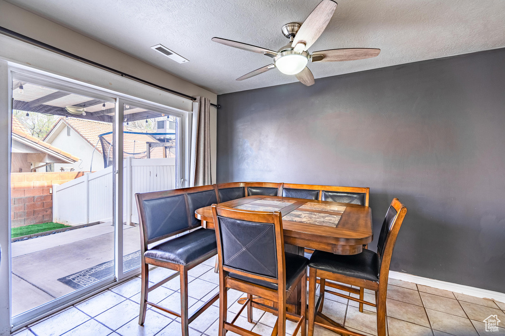 Dining space with light tile patterned flooring, a textured ceiling, visible vents, baseboards, and a ceiling fan