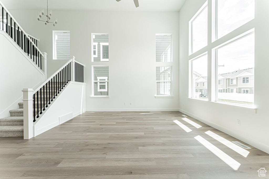 Unfurnished living room with stairway, plenty of natural light, light wood-style floors, and a chandelier