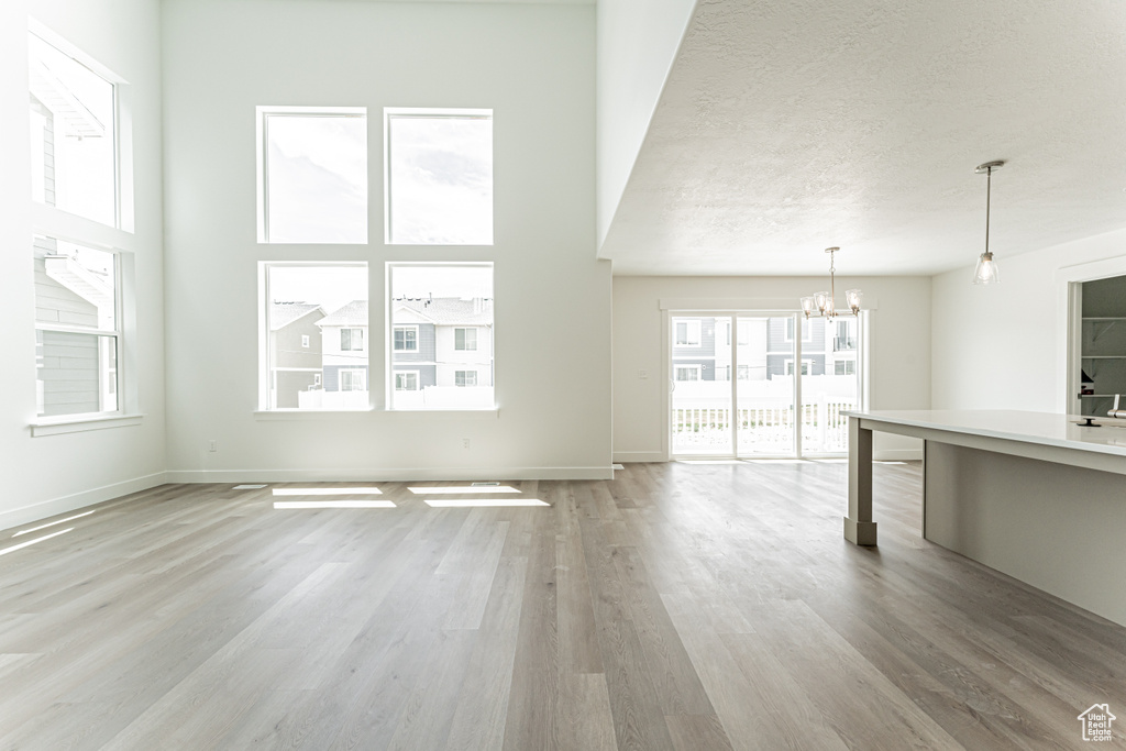 Unfurnished living room featuring a chandelier, light wood finished floors, and a textured ceiling