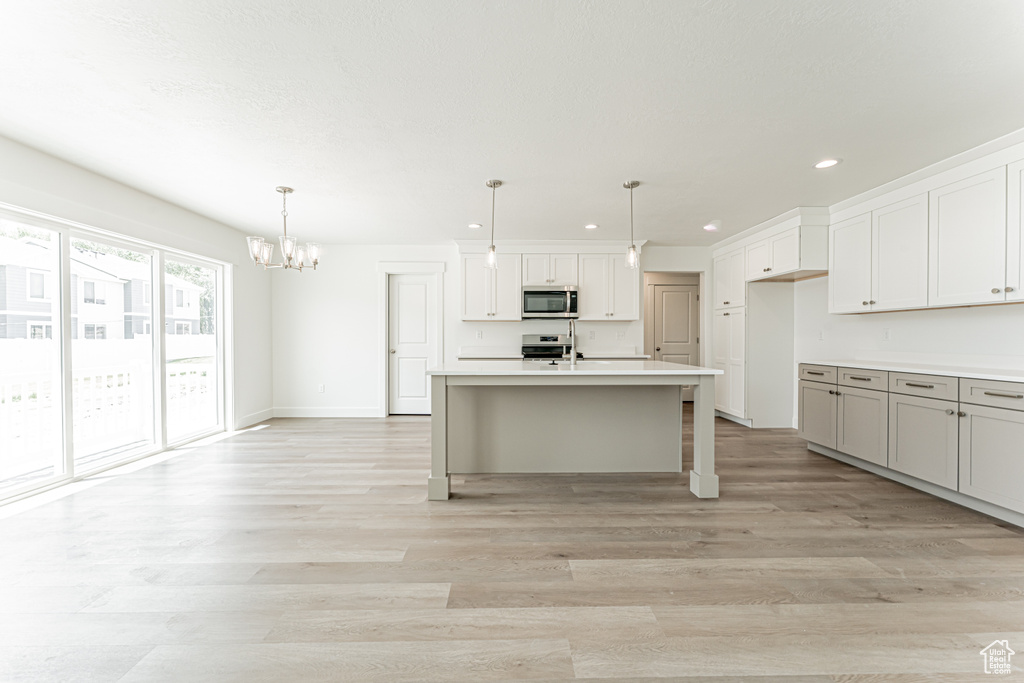 Kitchen featuring stainless steel microwave, recessed lighting, range, light wood-style flooring, and a chandelier