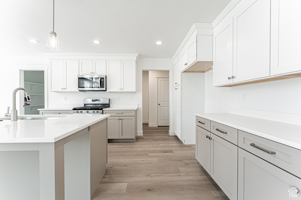 Kitchen featuring appliances with stainless steel finishes, recessed lighting, hanging light fixtures, light countertops, and light wood-style flooring