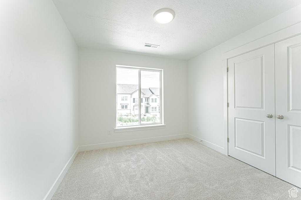 Unfurnished bedroom featuring carpet flooring, a textured ceiling, and a closet